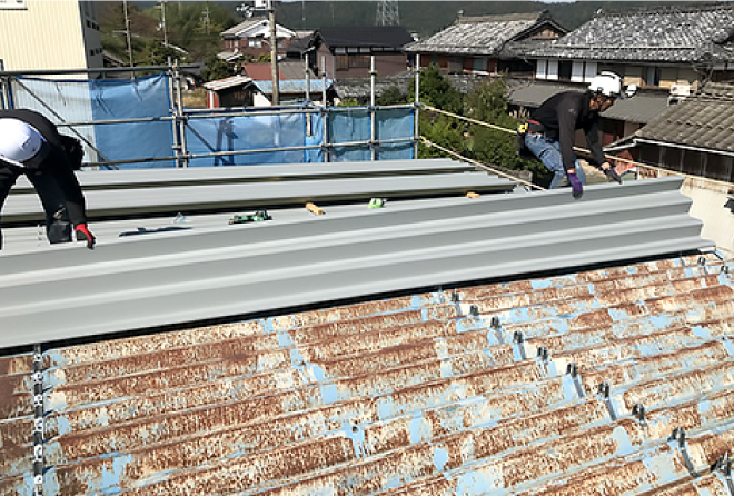 新しい屋根材を既存の屋根材の上から二人がかりで一枚一枚施工していきます