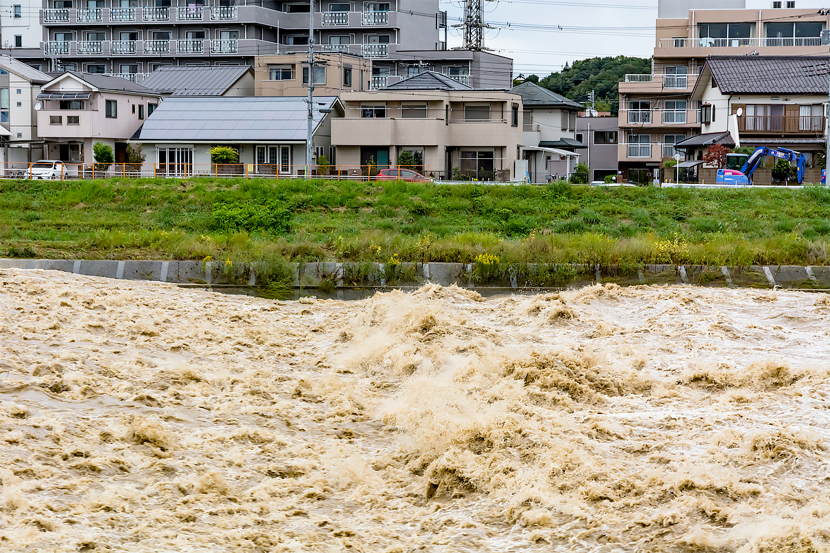台風で増水した川の後ろに住宅